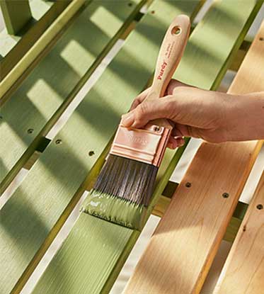 applying green paint to a bench